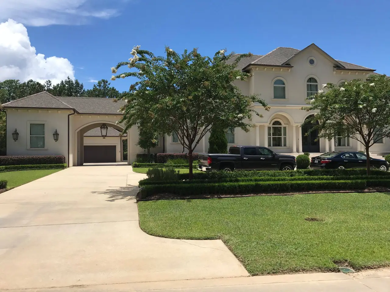 Two-story cream stucco home with arched windows and an arched carriage entry